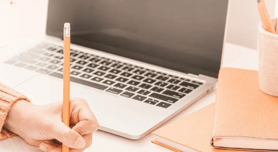 Experienced writer writing notes for a business award on a note pad in front of laptop